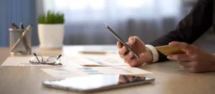 A man typing on a mobile phone while looking at a credit card